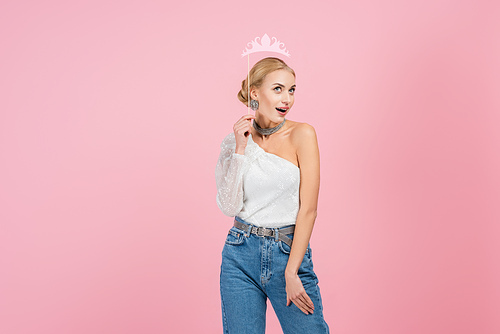 amazed and stylish woman holding paper crown on stick isolated on pink