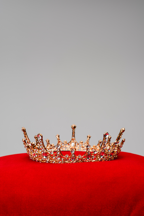 golden royal crown on red velvet cushion isolated on grey