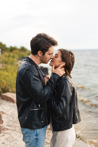 Side view of couple in leather jackets kissing on seaside