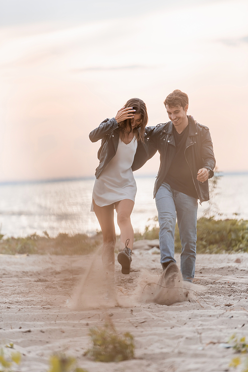 Selective focus of young couple throwing sand on sea cost at sunset
