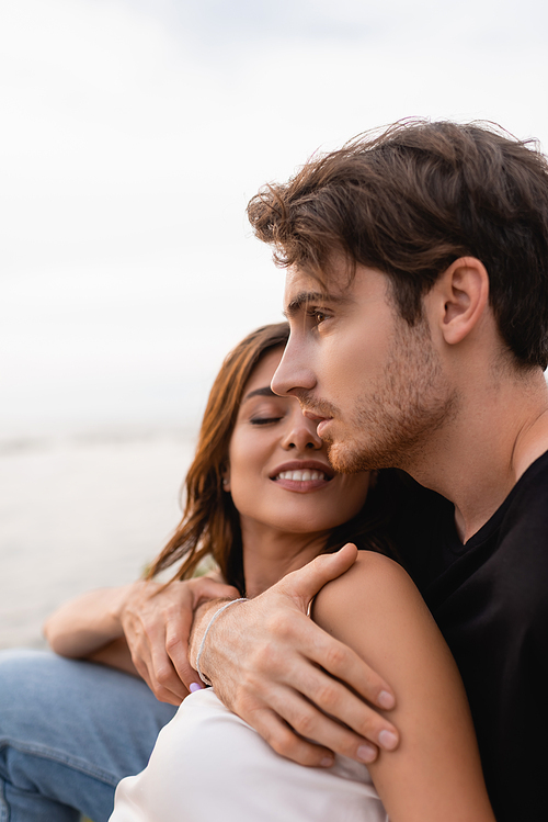 Man embracing girlfriend with closed eyes near sea