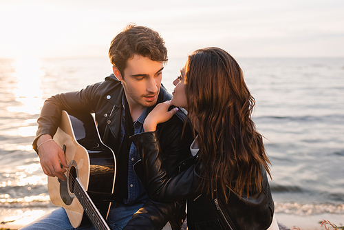 Young woman looking at boyfriend with acoustic guitar on beach at sunset