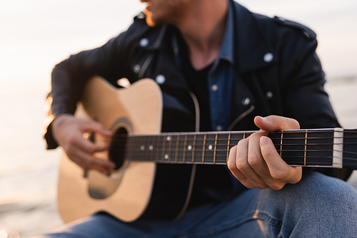 Cropped view of young man playing acoustic guitar outdoors