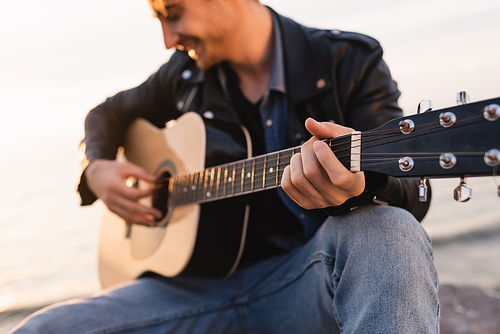 Selective focus of man playing acoustic guitar outdoors