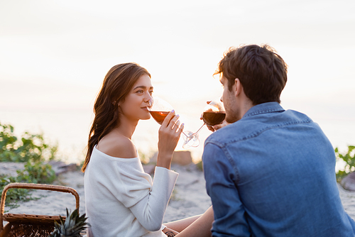 Selective focus of woman drinking wine with boyfriend during picnic on beach