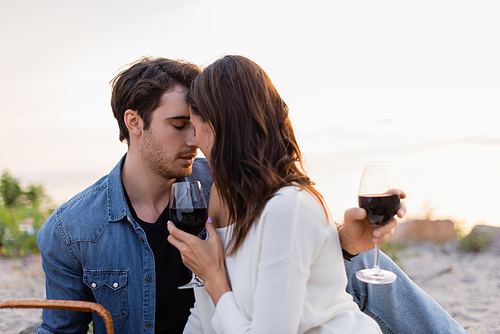 Young couple with glasses of wine kissing on beach at sunset