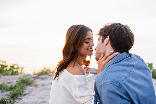 Selective focus of woman with glass of wine kissing boyfriend on beach