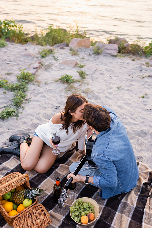 Overhead view couple with wine and acoustic guitar kissing on beach at evening