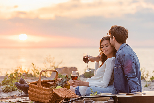 Selective focus of couple holding glasses of wine during picnic on beach at evening