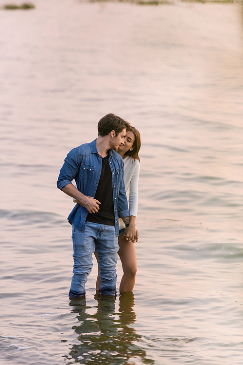Young couple holding hands while standing in sea water at sunset