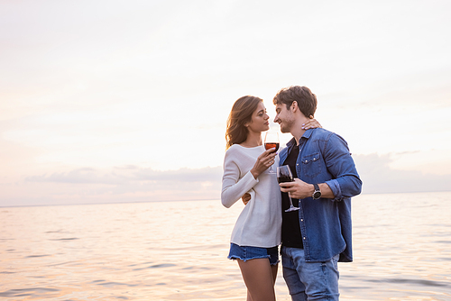 Young woman holding glass of wine and touching boyfriend near sea