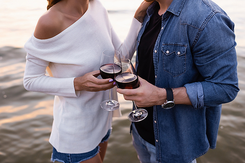 Cropped view of young couple holding glasses of wine near sea