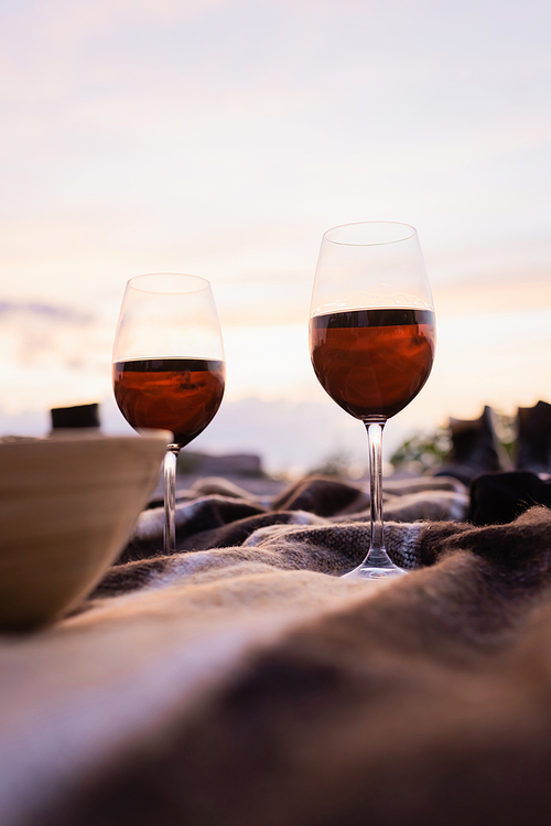 Selective focus of glasses of wine near bowl on blanket outside