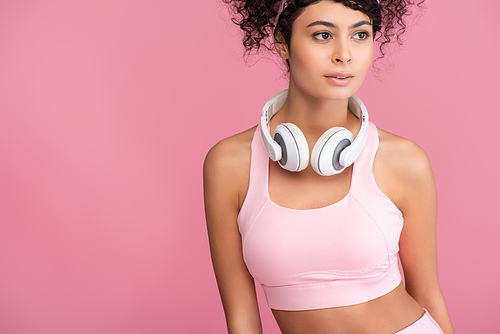 curly young woman in wireless headphones looking away isolated on pink