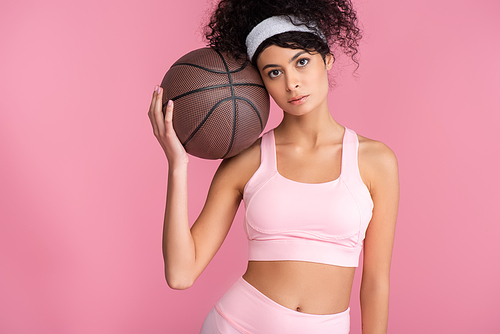 curly young woman holding basketball while  isolated on pink