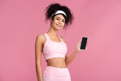 happy sportswoman holding smartphone with blank screen isolated on pink