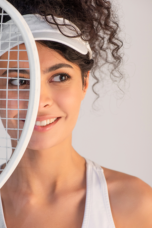 cheerful player in cap looking away near tennis racket isolated on white