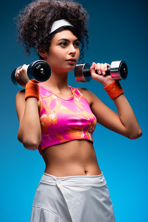 curly young woman exercising with dumbbells on blue