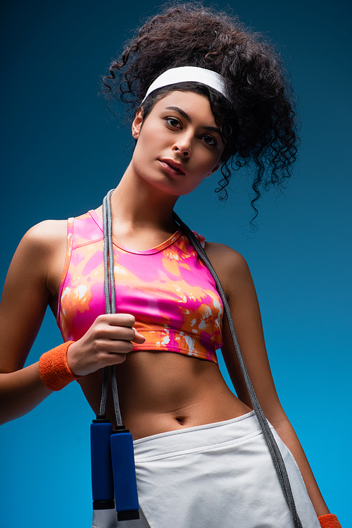 curly young woman standing with skipping rope on blue