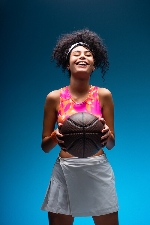 smiling woman in sportswear holding basketball on blue