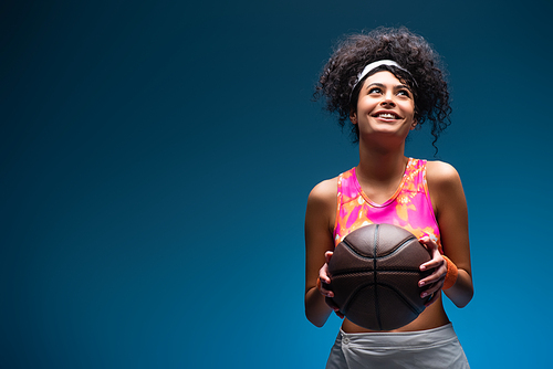 cheerful woman in sportswear holding basketball on blue