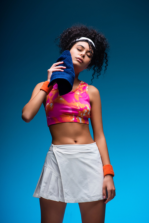 tired woman in sportswear wiping sweat with towel on blue