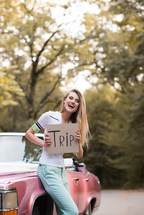 excited woman holding card with trip lettering near vintage cabriolet
