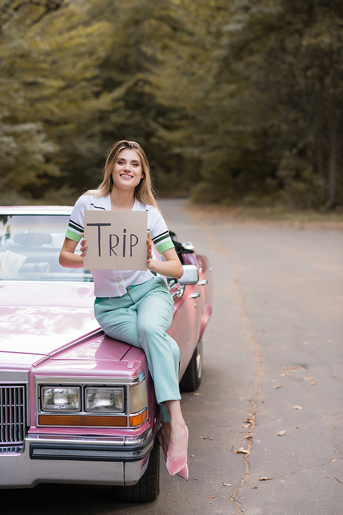 smiling stylish woman  while sitting on cabriolet hood