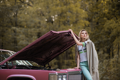 young woman looking away while opening hood of broken retro car