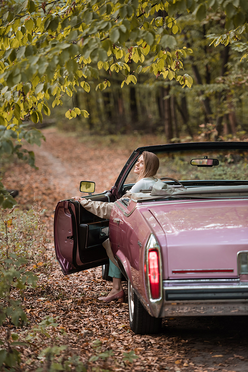 young woman in coat opening door while sitting in vintage cabriolet