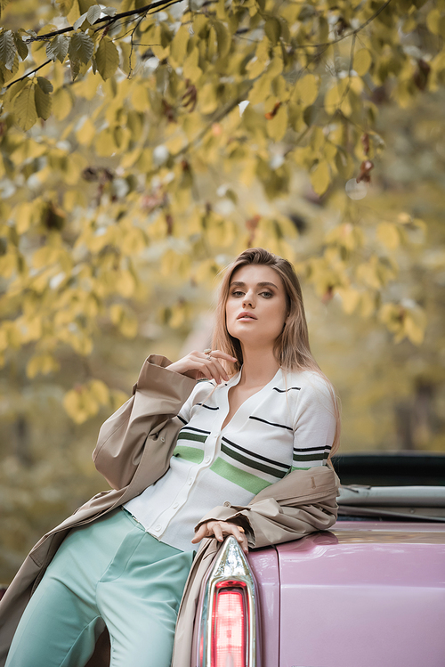 young stylish woman in cape  while posing near cabriolet in forest