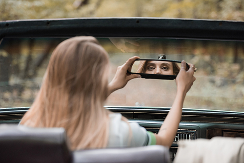 back view of young woman adjusting rearview mirror in cabriolet on blurred foreground