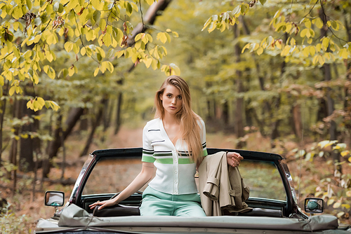 young stylish woman  and holding cape while sitting in vintage cabriolet