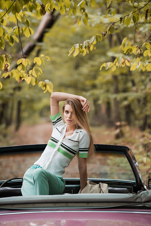 stylish woman with hand above head  while posing in cabriolet