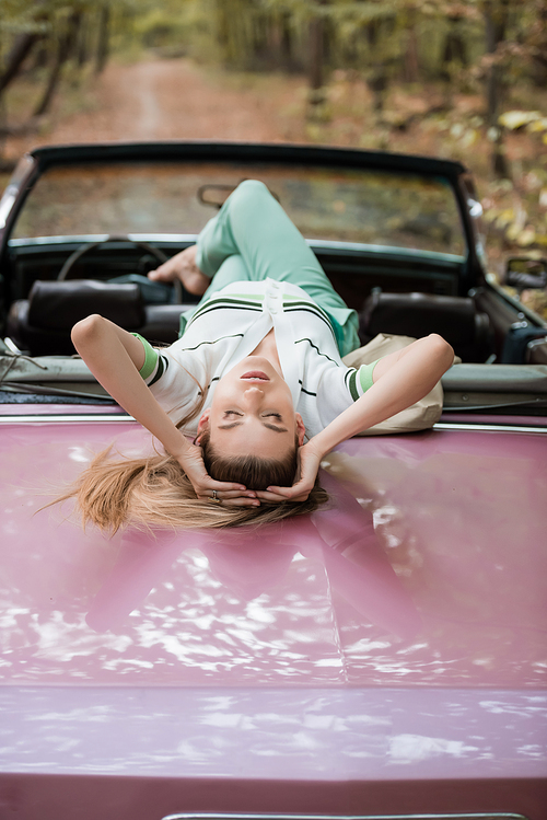 young woman relaxing while lying on cabriolet with closed eyes on blurred background