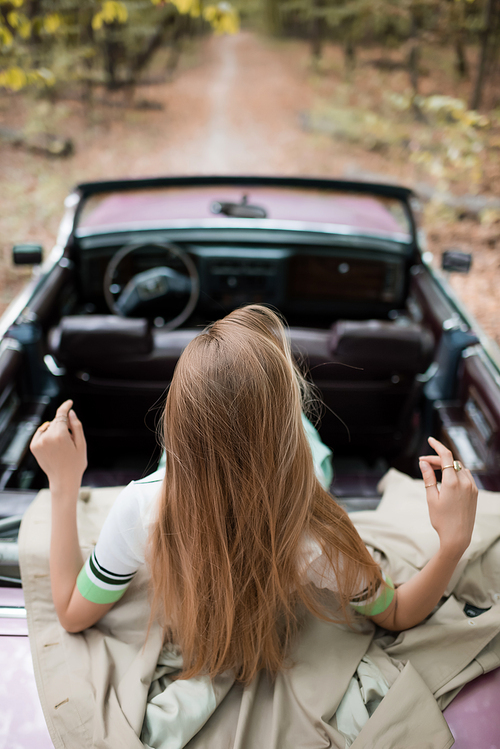 back view of young woman sitting in vintage cabriolet on blurred background