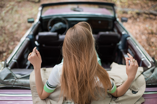 back view of young woman sitting in vintage convertible car on blurred background