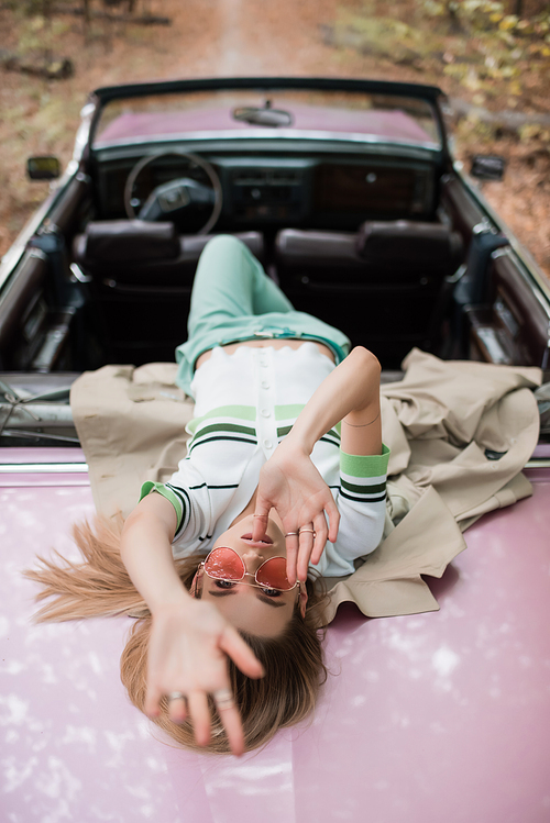 overhead view of young woman  while lying on cabriolet on blurred background