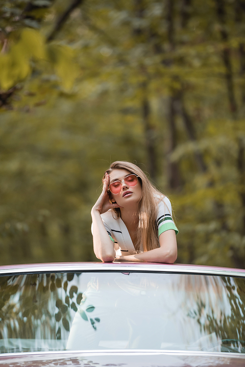 young woman with closed eyes touching head while standing in convertible car