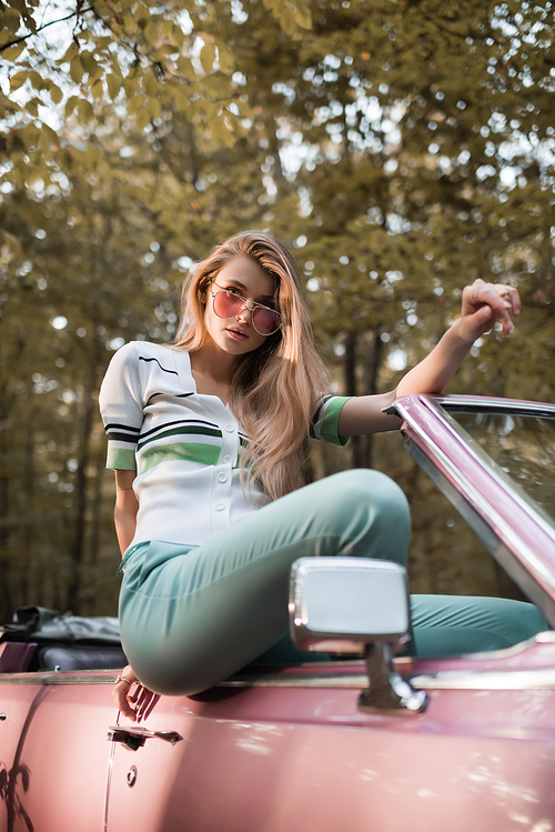 stylish woman in sunglasses  while posing in cabriolet on blurred foreground