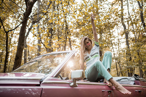 joyful barefoot woman  while posing with hand in air in cabriolet