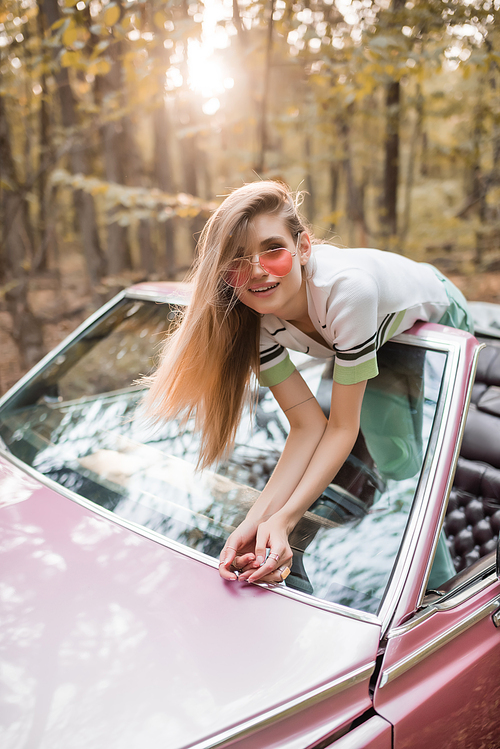 stylish woman in sunglasses leaning on windshield of cabriolet and 