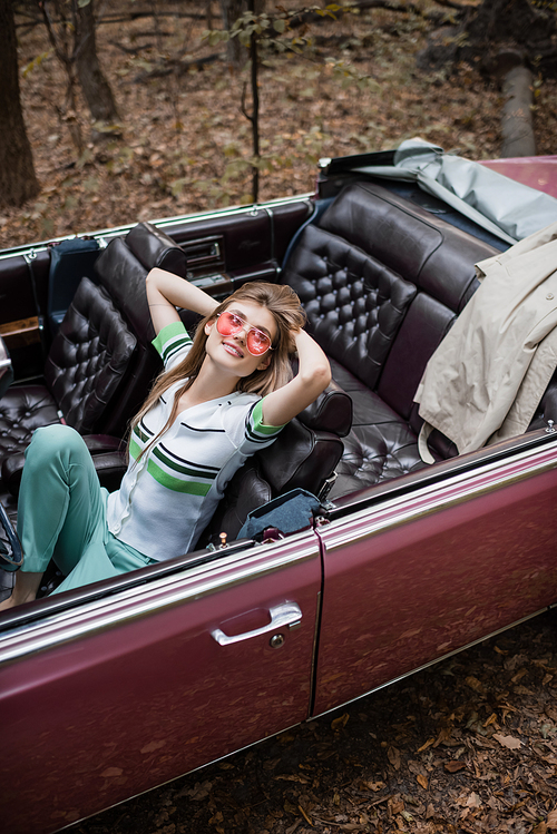 high angle view of joyful woman relaxing while sitting in vintage cabriolet with hands behind head