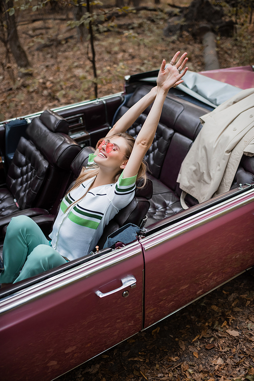 high angle view of cheerful woman relaxing while sitting in retro cabriolet and stretching hands