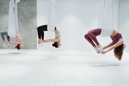 side view of three young women practicing aerial yoga in gym