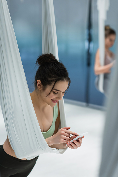 Cheerful woman using mobile phone during fly yoga training