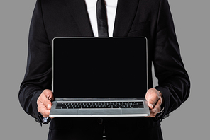 cropped view of businessman in black suit showing laptop with blank screen isolated on grey