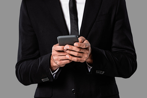 partial view of businessman in black suit using smartphone isolated on grey