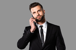 dreamy handsome businessman in black suit talking on smartphone isolated on grey