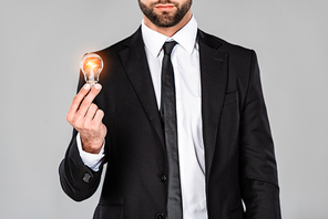 cropped view of businessman in black suit holding glowing light bulb isolated on grey